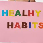 A woman holds a pink poster with colorful letters spelling 'HEALTHY HABITS'.