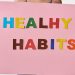 A woman holds a pink poster with colorful letters spelling 'HEALTHY HABITS'.